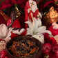 May include: A brown coconut bowl filled with dried herbs and flowers. The bowl is sitting on a red surface with a white flower, red flowers, and two dice.